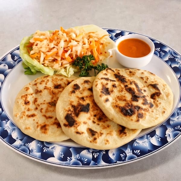 Three pupusas with curtido and red sauce on a blue and white patterned plate.