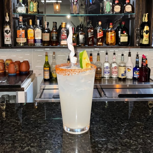 A margarita with a chili-lime rim and lime wedge sits on a dark granite bar top.