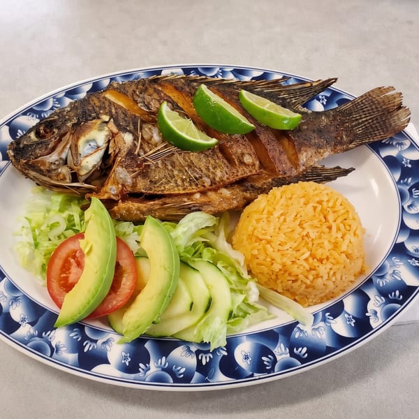 Whole fried fish with lime wedges, a side of rice, and a salad with avocado and tomato.