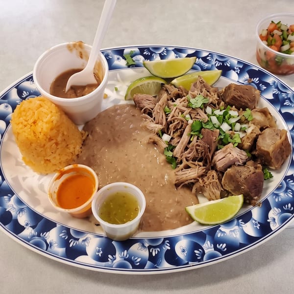 A plate of carnitas with rice, refried beans, lime wedges, and small cups of salsa.