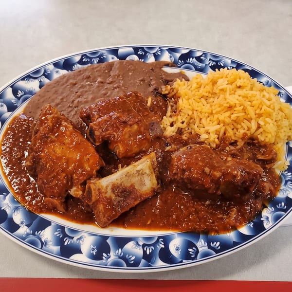 Pork ribs in red sauce, refried beans, and yellow rice on a blue and white patterned plate.