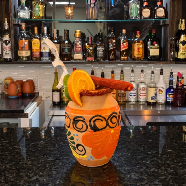 A colorful, decorated clay pot cocktail with orange, lime, and chili candy on a bar.